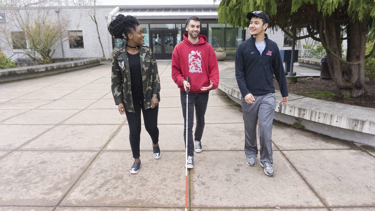 Students walking together talking outside. One student is using a white cane.