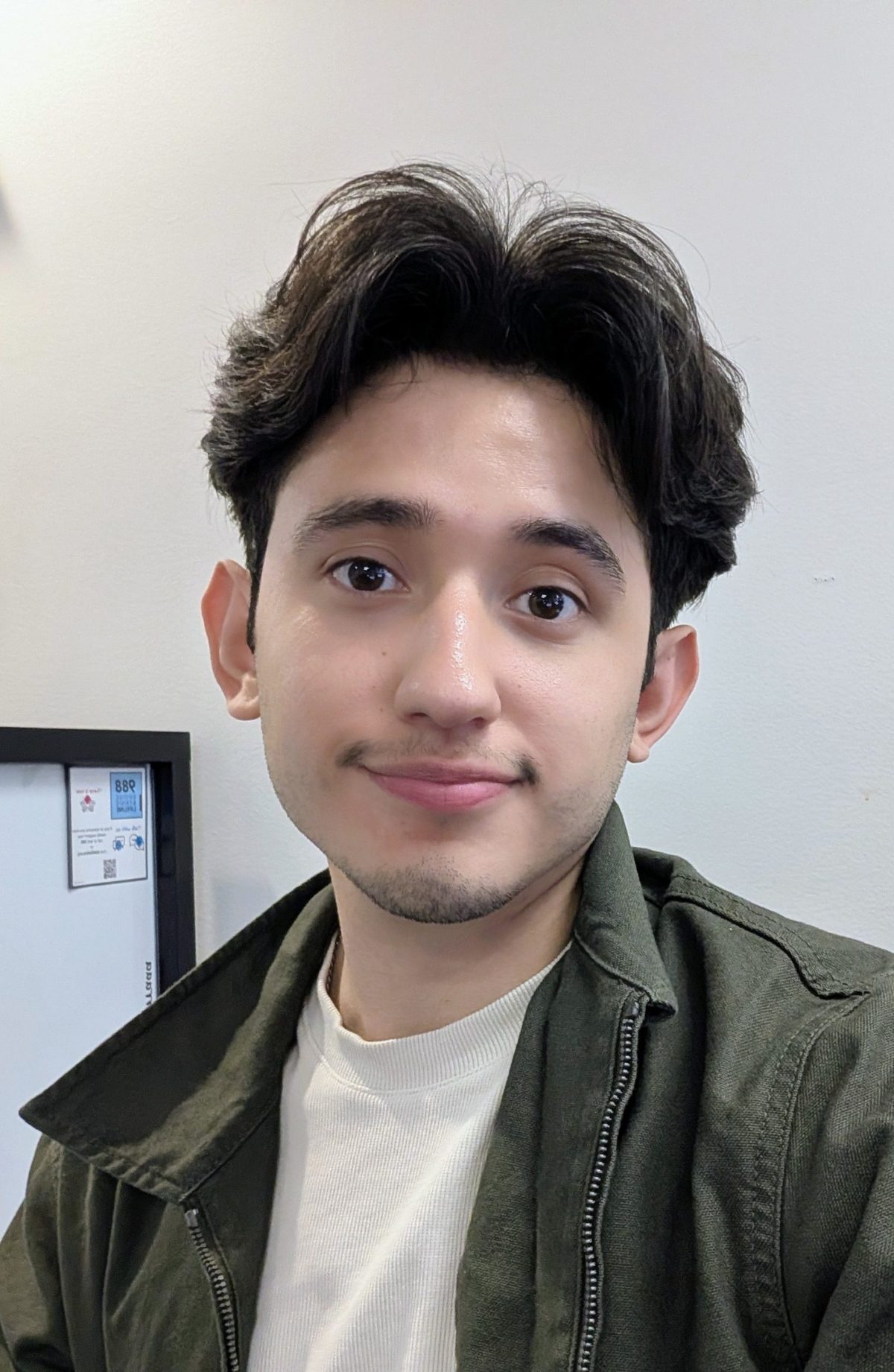 Picture of a young man with light brown skin and short dark hair. He is looking into the camera and smiling.