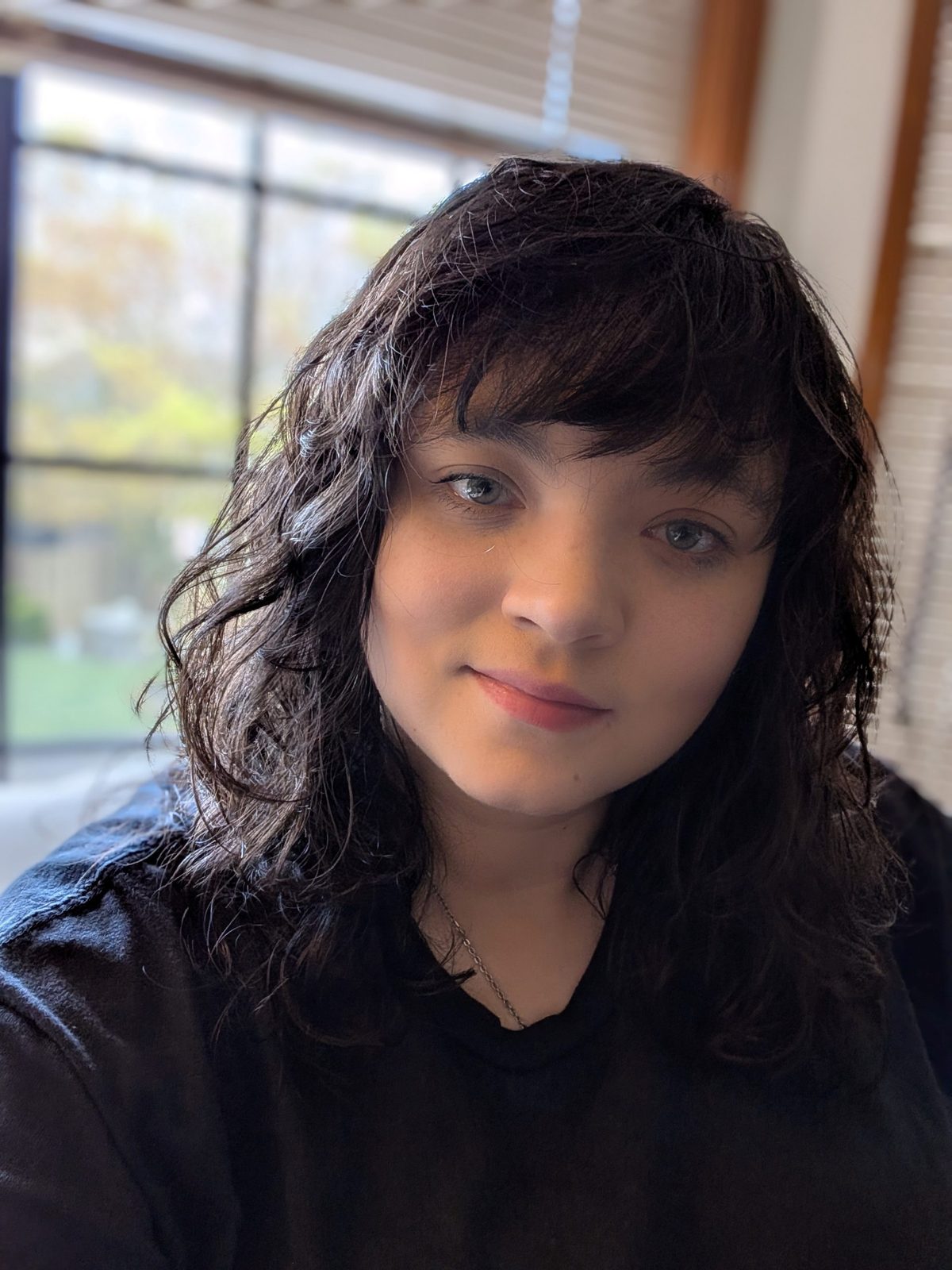 Picture of a woman with light brown skin and dark curly shoulder-length hair. She is smiling slightly.