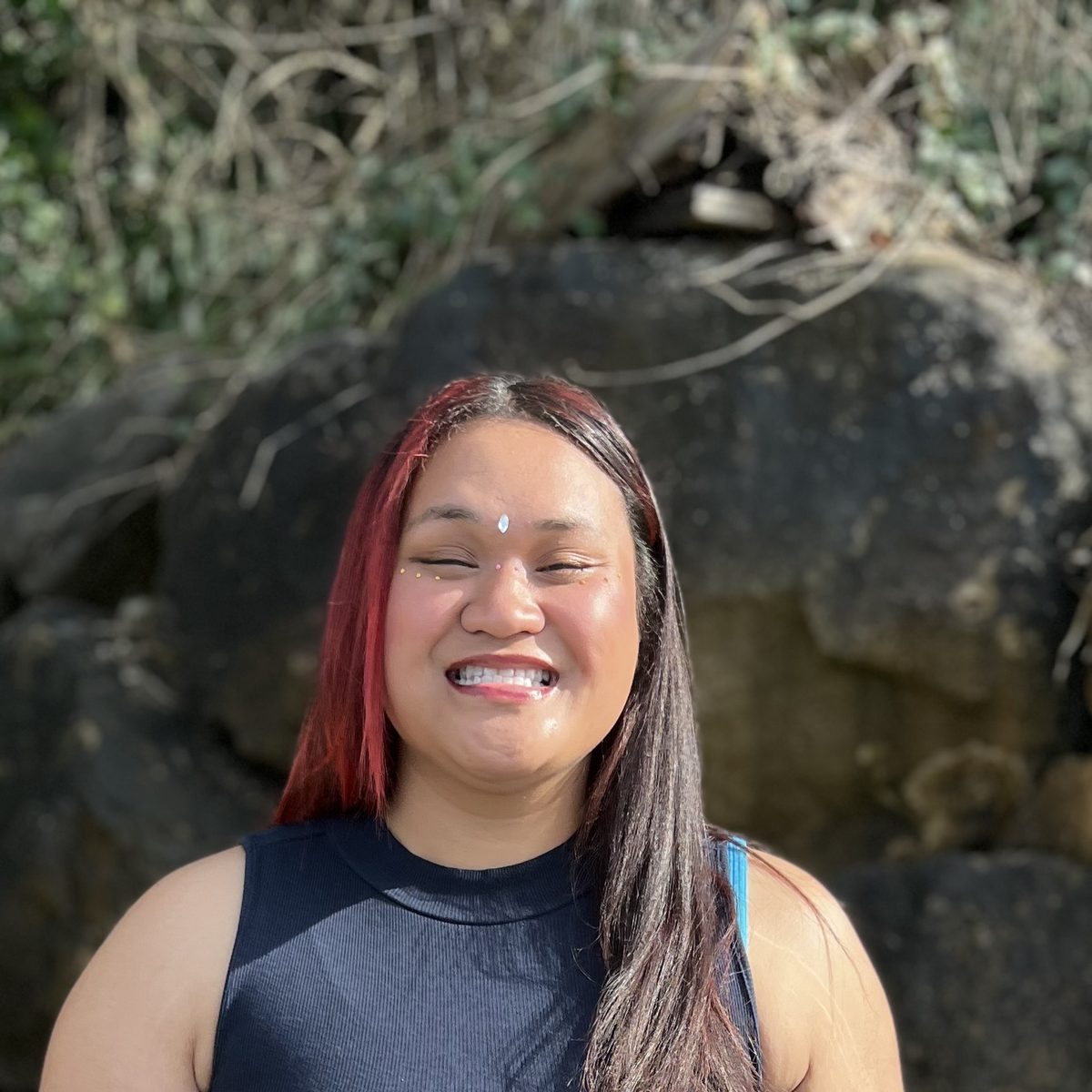 Picture of a women with medium brown skin and long brown and red hair. She is smiling.