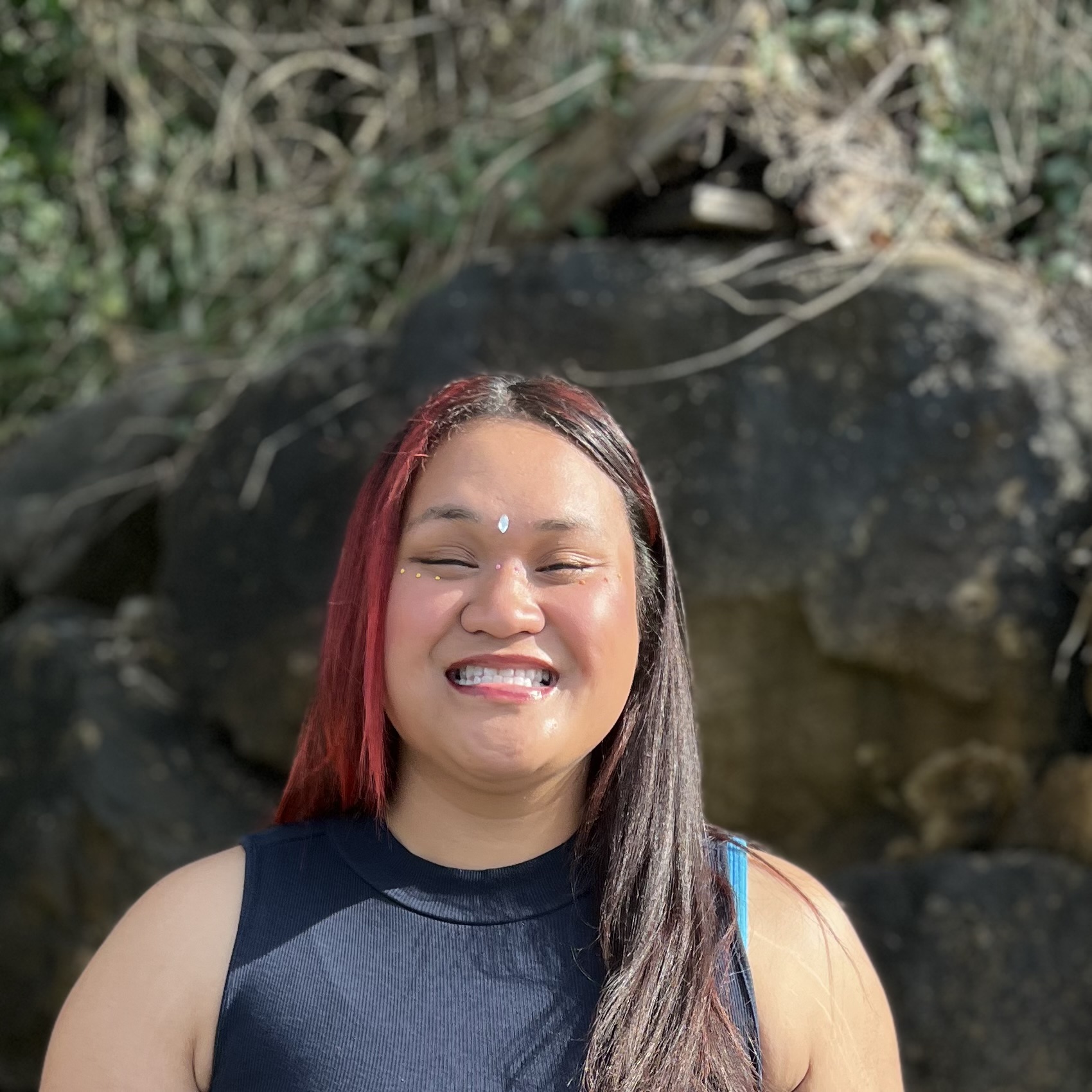 Picture of a women with medium brown skin and long brown and red hair. She is smiling.